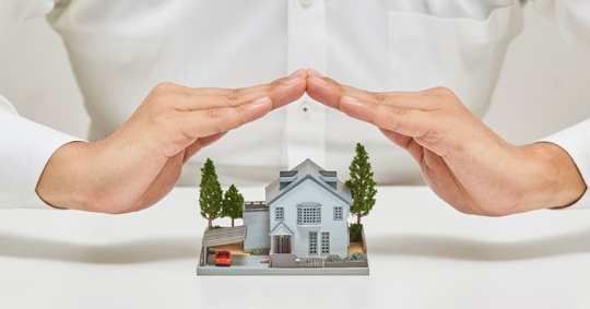 Hands Protecting a Miniature Model of a House and a Car
