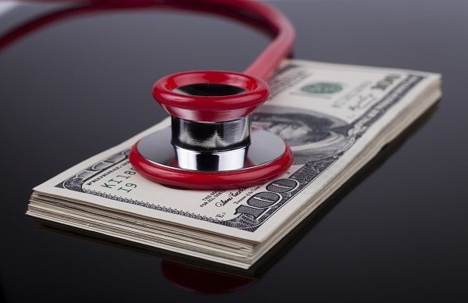 Red stethoscope on top of a stack of $100 bills